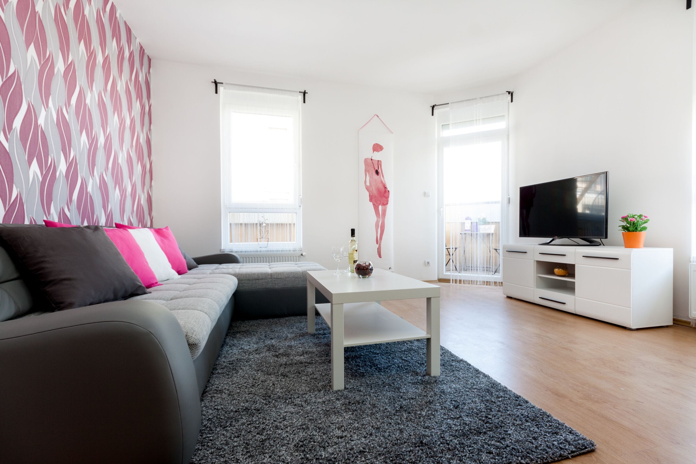 Un salon moderne avec un canapé gris, une table basse blanche et un téléviseur à écran plat posé sur un meuble blanc.