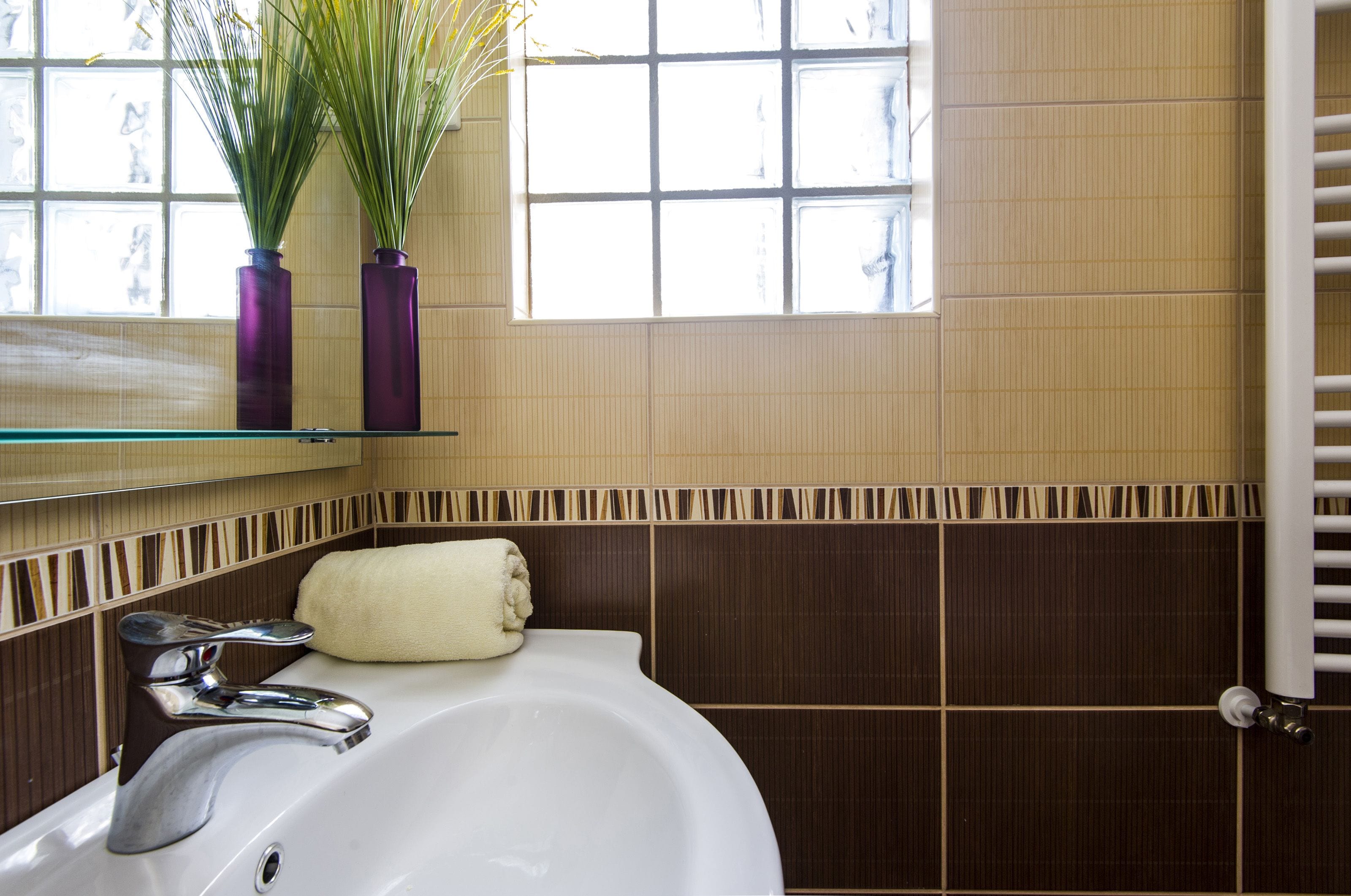 Une salle de bain avec un lavabo blanc, une serviette et deux vases violets posés sur une étagère en verre.
