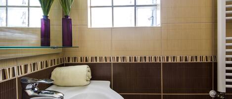 Une salle de bain avec un lavabo blanc, une serviette et deux vases violets posés sur une étagère en verre.