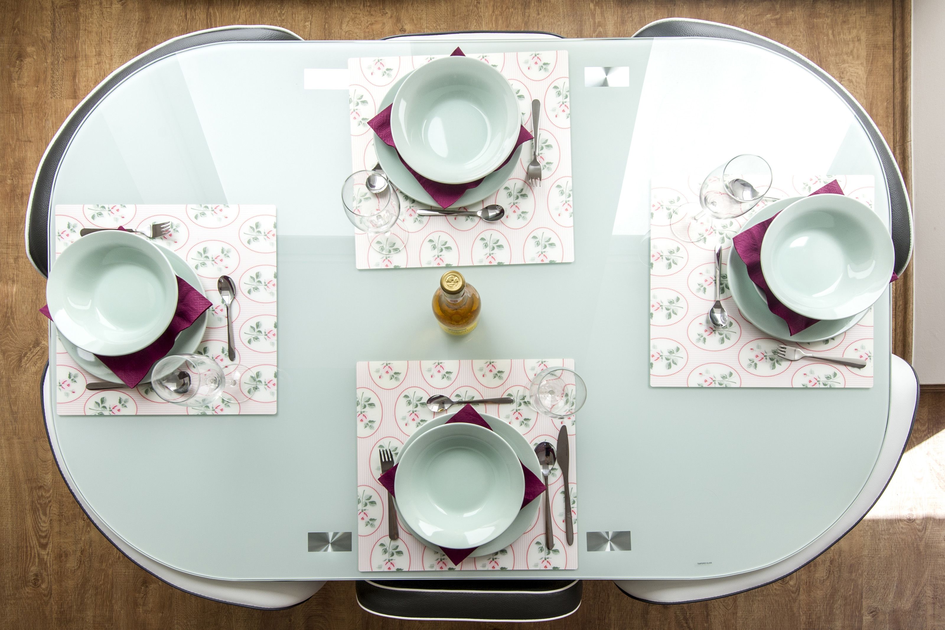A dining table set with four plates, cutlery, and glasses, centered on a patterned table runner.
