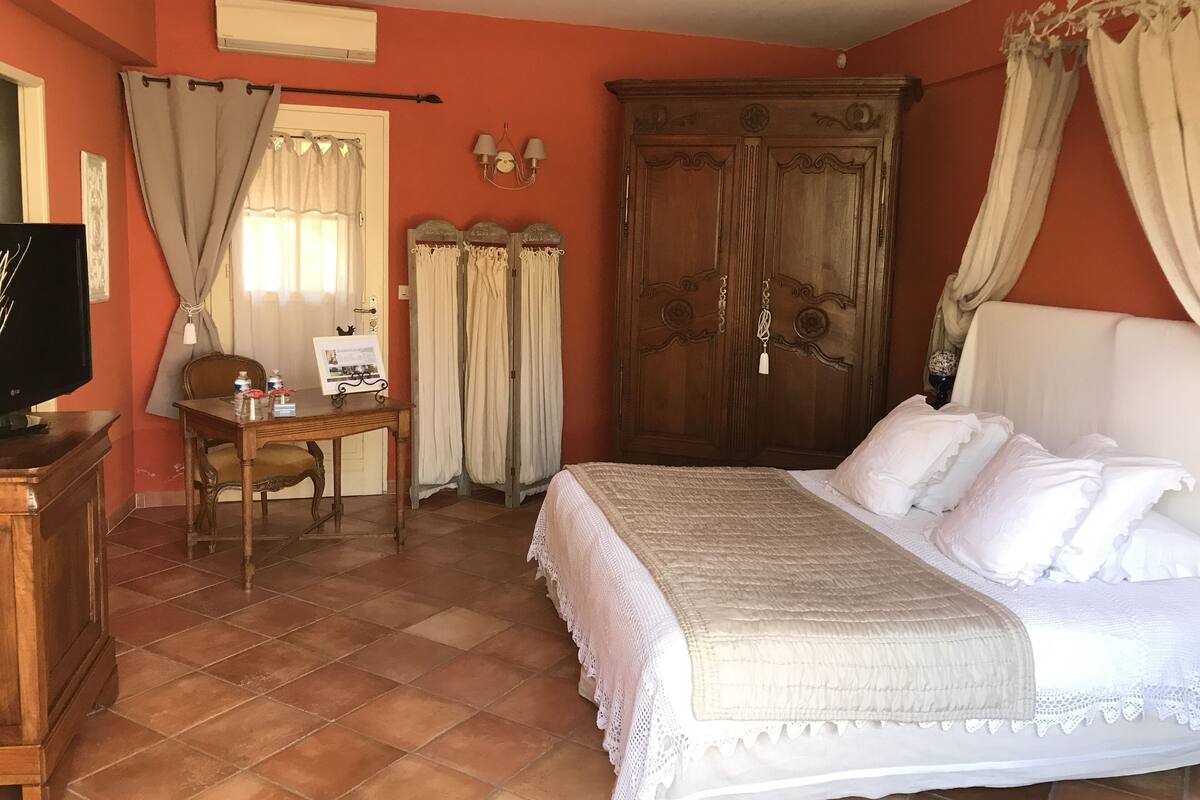 Een slaapkamer met een bed, een houten garderobe, een bureau met stoel, en een televisie.
