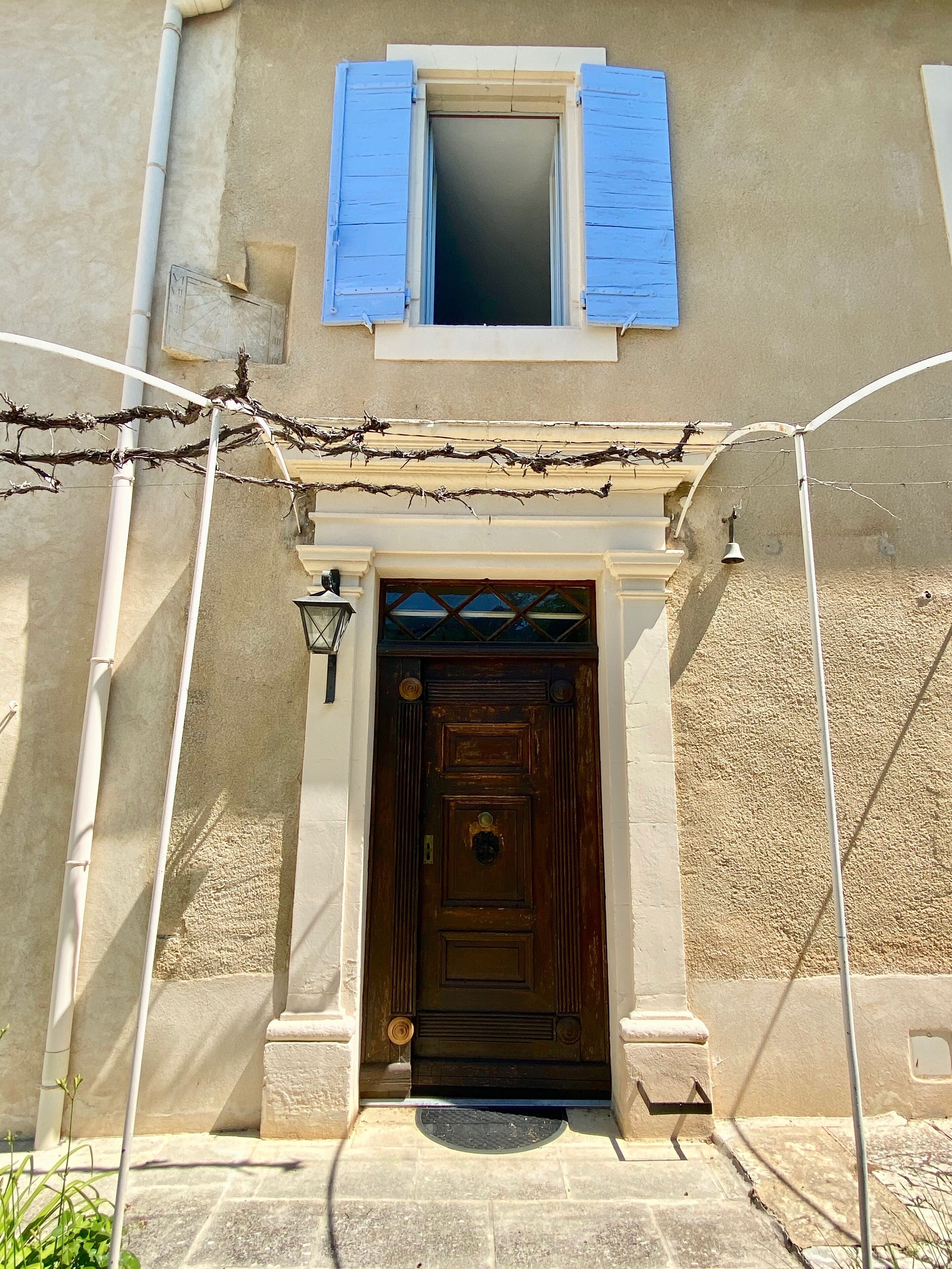 Un bâtiment avec une porte en bois, une fenêtre avec des volets bleus et un petit balcon doté d’une rambarde en métal.
