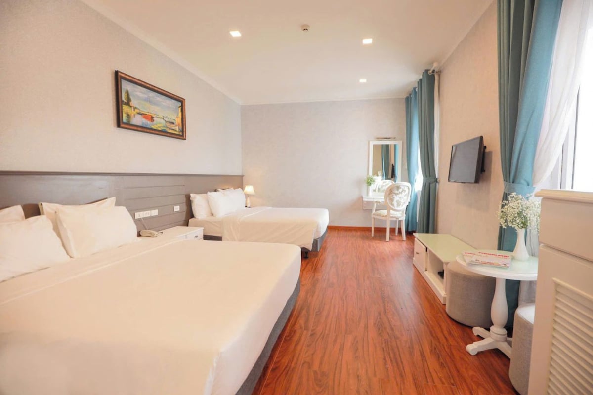 A hotel room with two beds, a desk, a chair, a television, and a painting on the wall.