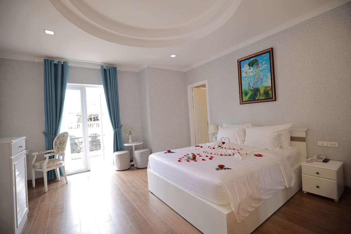 Quarto de hotel com uma cama grande, uma escrivaninha, uma cadeira e uma varanda com cortinas.