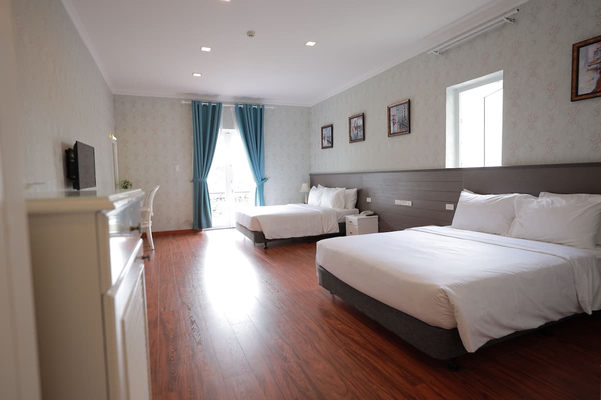 Quarto de hotel com duas camas, uma escrivaninha e uma janela com cortinas.