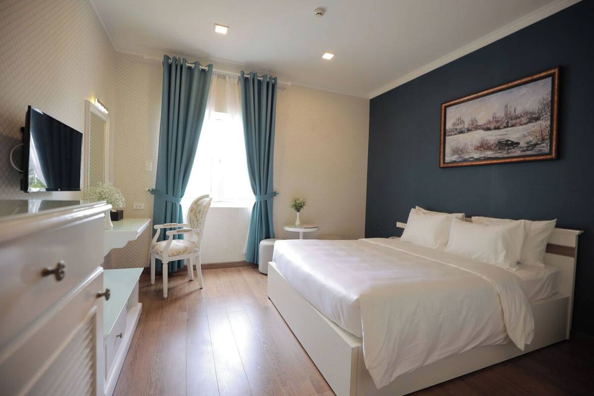 Quarto com cama, cadeira, escrivaninha, televisão e um quadro na parede.