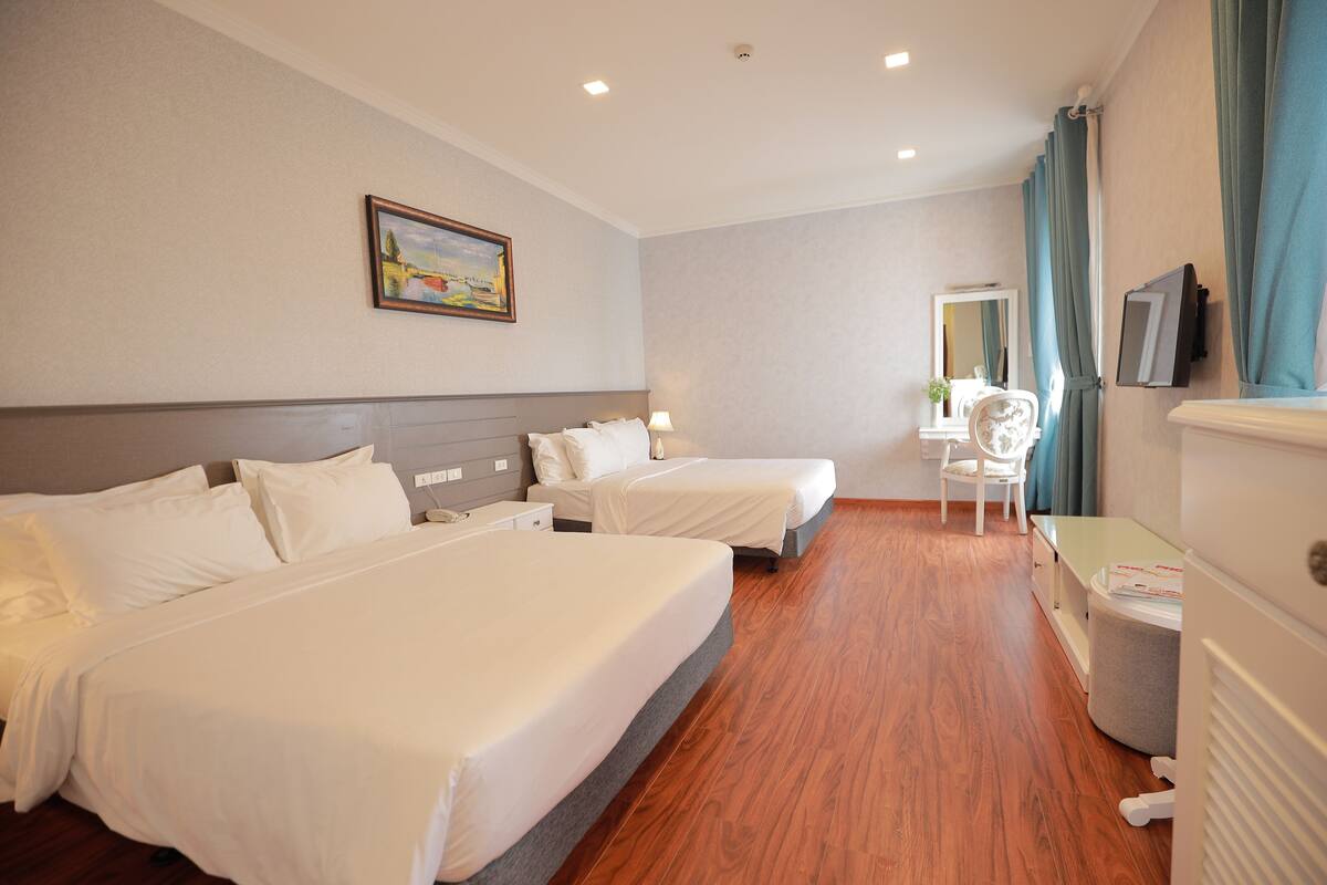 Quarto de hotel com duas camas, uma mesa, uma cadeira, uma TV e uma janela com cortinas.