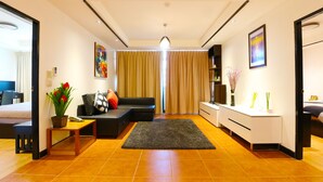 A modern living room with a sofa, a coffee table, and a rug. There is a desk with a vase and a picture frame. - Serena Sathorn Suites (Bangkok)