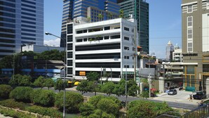 A modern building with multiple floors, surrounded by greenery and other urban structures. - Serena Sathorn Suites (Bangkok)