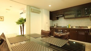 A modern kitchen with dark cabinets, a glass dining table, and a built-in microwave. - Serena Sathorn Suites (Bangkok)