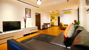 A modern living room with a flat-screen TV, a sofa, a coffee table, and a dining area in the background. - Serena Sathorn Suites (Bangkok)
