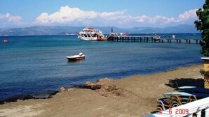 A coastal scene with a pier extending into the sea, a boat docked at the pier, and a small boat in the water. - Lemon Grove Hotel and Studios (Corfu)