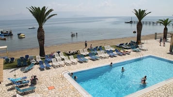 Ein Poolbereich mit Liegestühlen und Schwimmbecken mit Blick auf einen Strand, auf dem Boote und Palmen zu sehen sind.