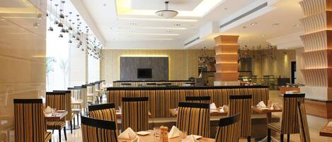 A modern restaurant with striped chairs, a central dining table, and a kitchen in the background.
