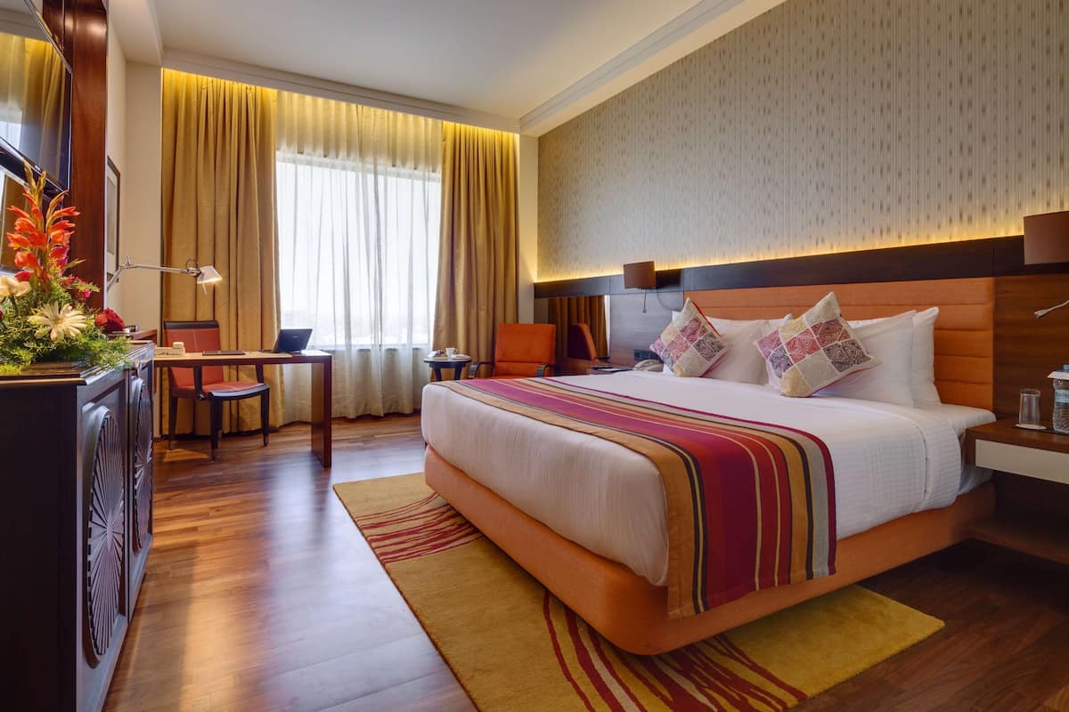 A hotel room with a large bed, a desk, a chair, a TV, and a window with curtains.