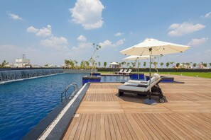 A poolside area with lounge chairs and umbrellas, a wooden deck, and a clear view of the surrounding landscape. - Balaji Sarovar Premiere Solapur (Solapur)