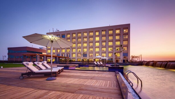 A hotel pool area with lounge chairs and umbrellas, a wooden deck, and a large building in the background. - Balaji Sarovar Premiere Solapur (Solapur)
