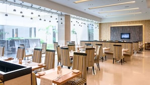 A modern dining area with striped chairs and tables, a bar area, and large windows offering a view of the outdoors. - Balaji Sarovar Premiere Solapur (Solapur)