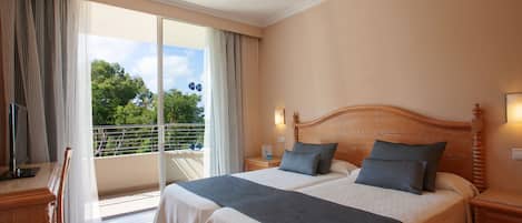 Une chambre d’hôtel avec deux lits, un balcon donnant sur la verdure et un bureau avec une chaise.