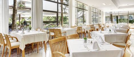 Un restaurante con varias mesas y sillas, ventanas amplias y vistas al exterior.