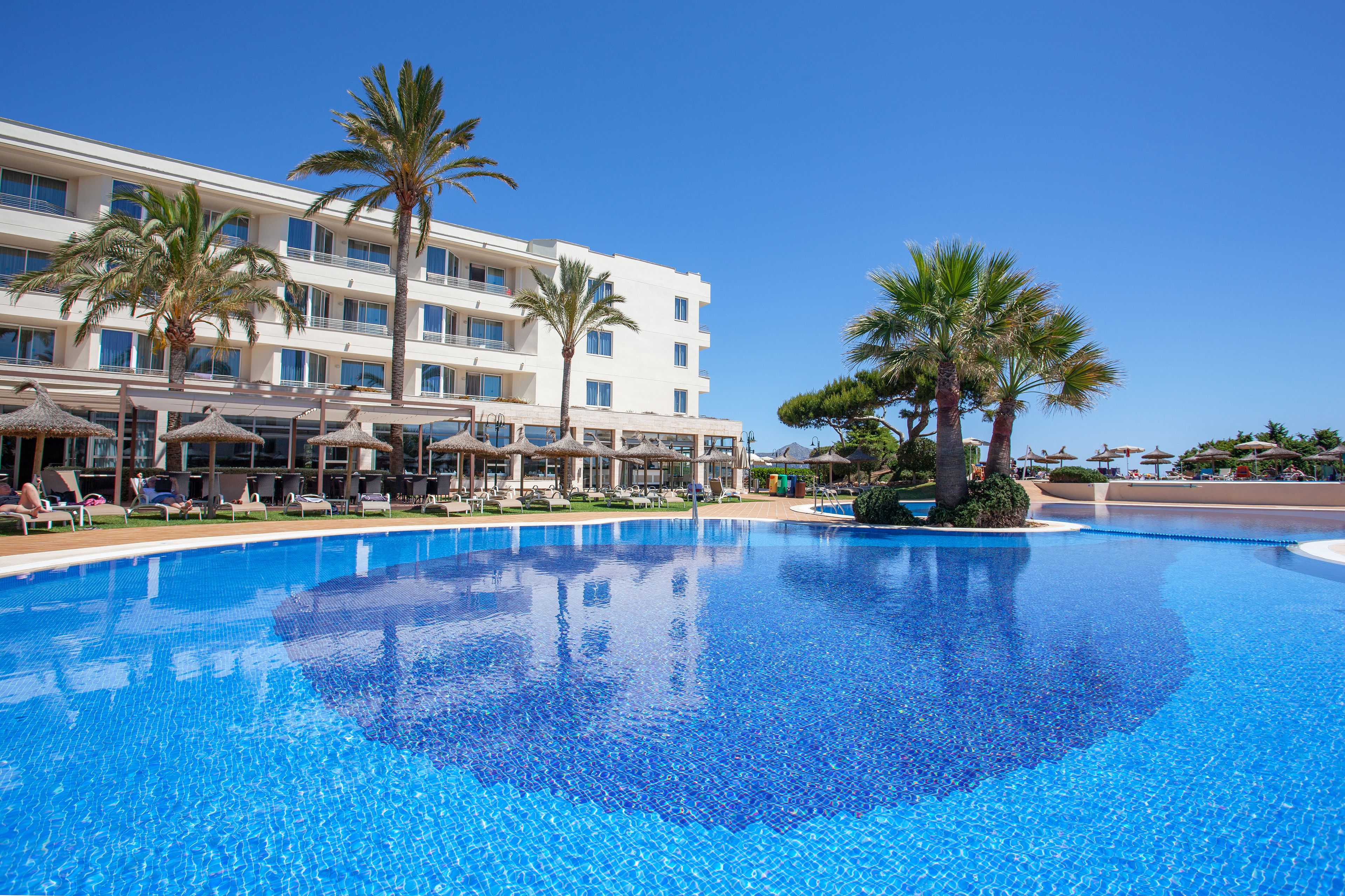 A hotel with a large swimming pool, palm trees, and lounge chairs.