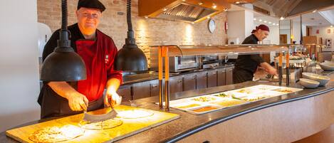 A buffet setup with a chef preparing food, a brick wall, and a modern kitchen in the background.