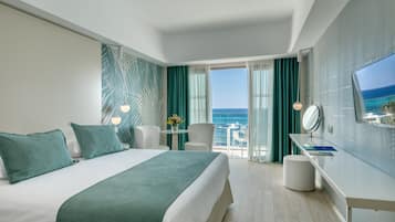 A hotel room with a bed, a desk, a chair, a TV, and a view of the ocean.