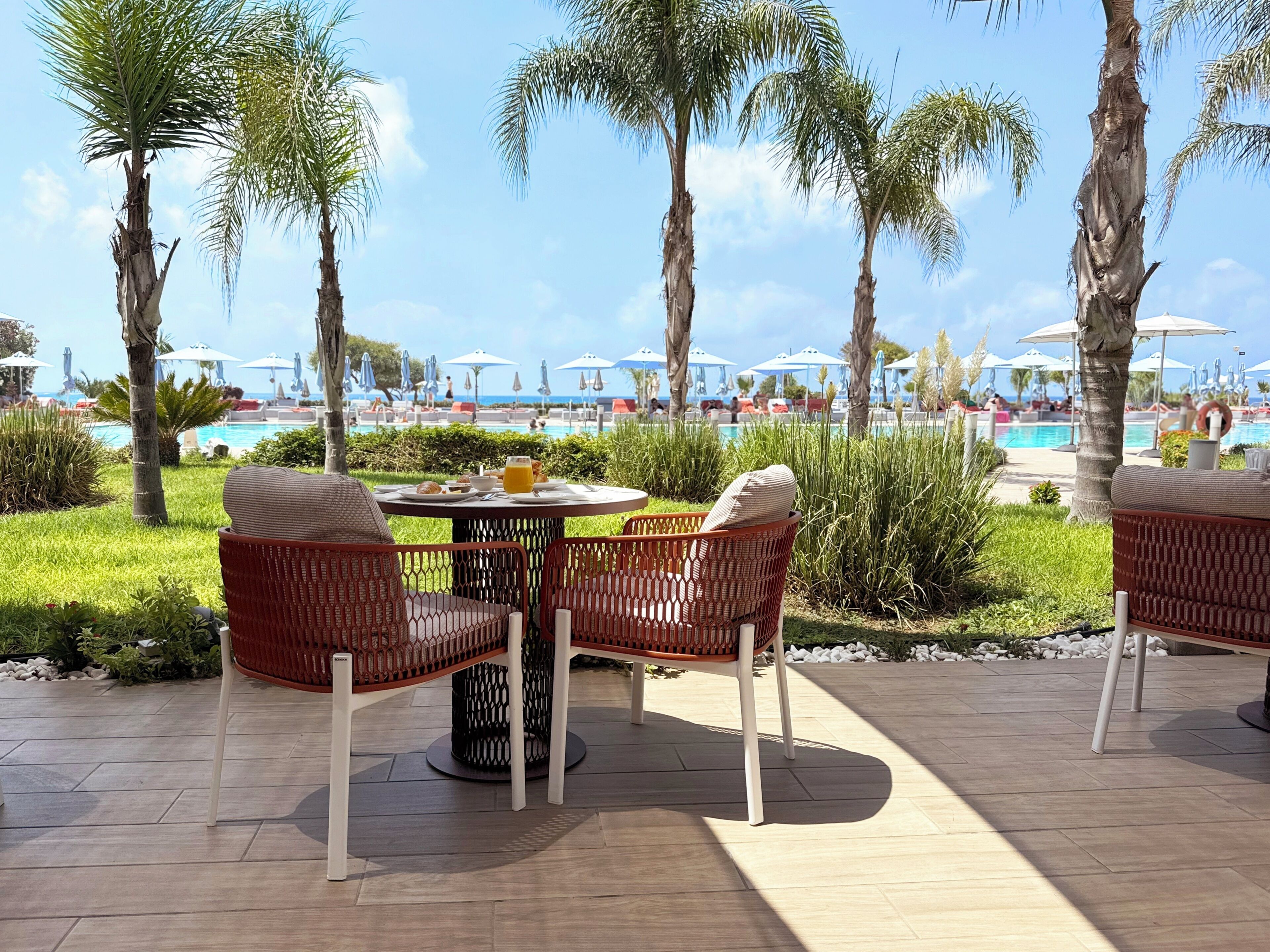 Un espace patio aménagé avec des chaises et une table en osier, donnant sur une piscine agrémentée de parasols.