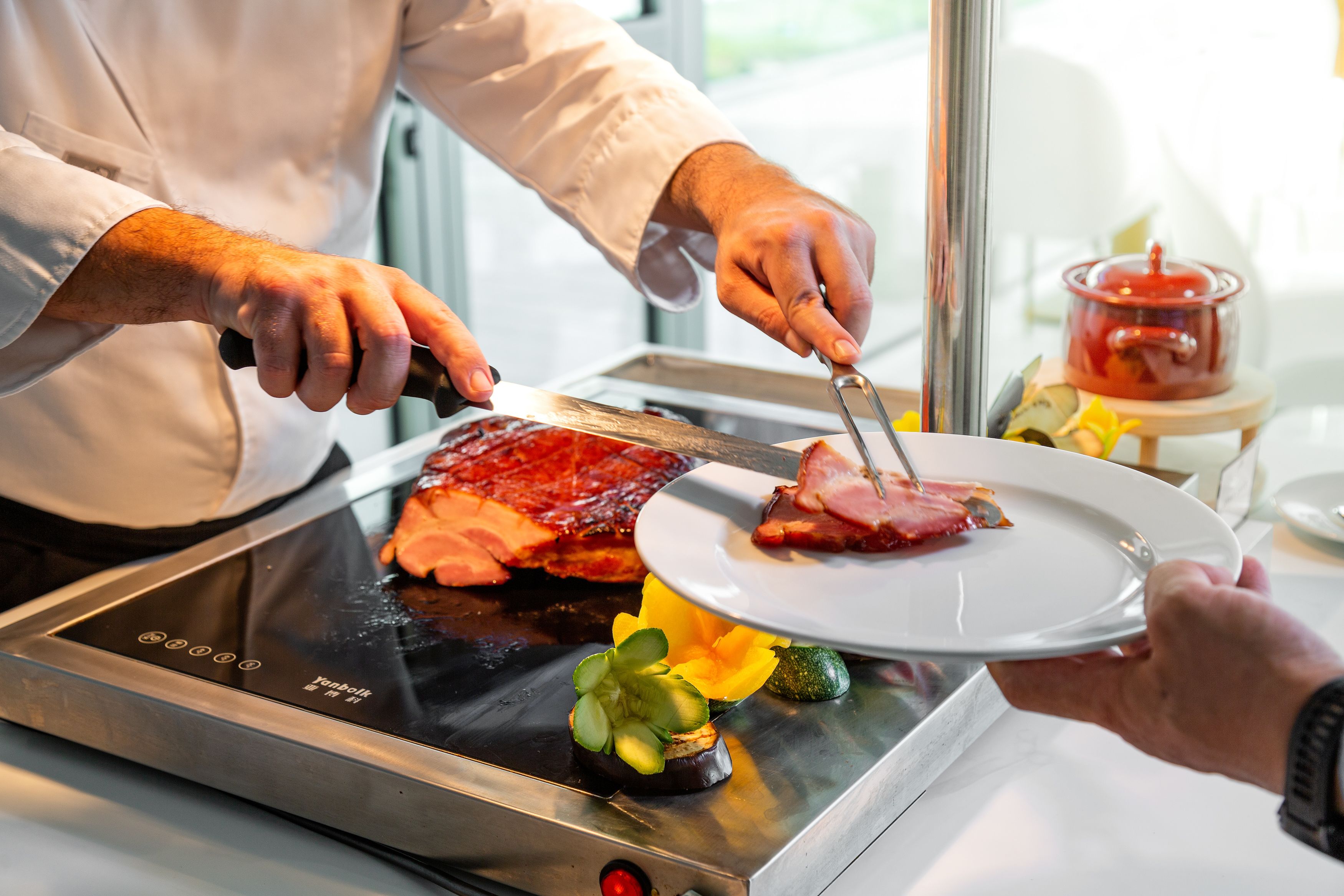 Una persona cortando carne en una parrilla, con un plato de verduras cerca.