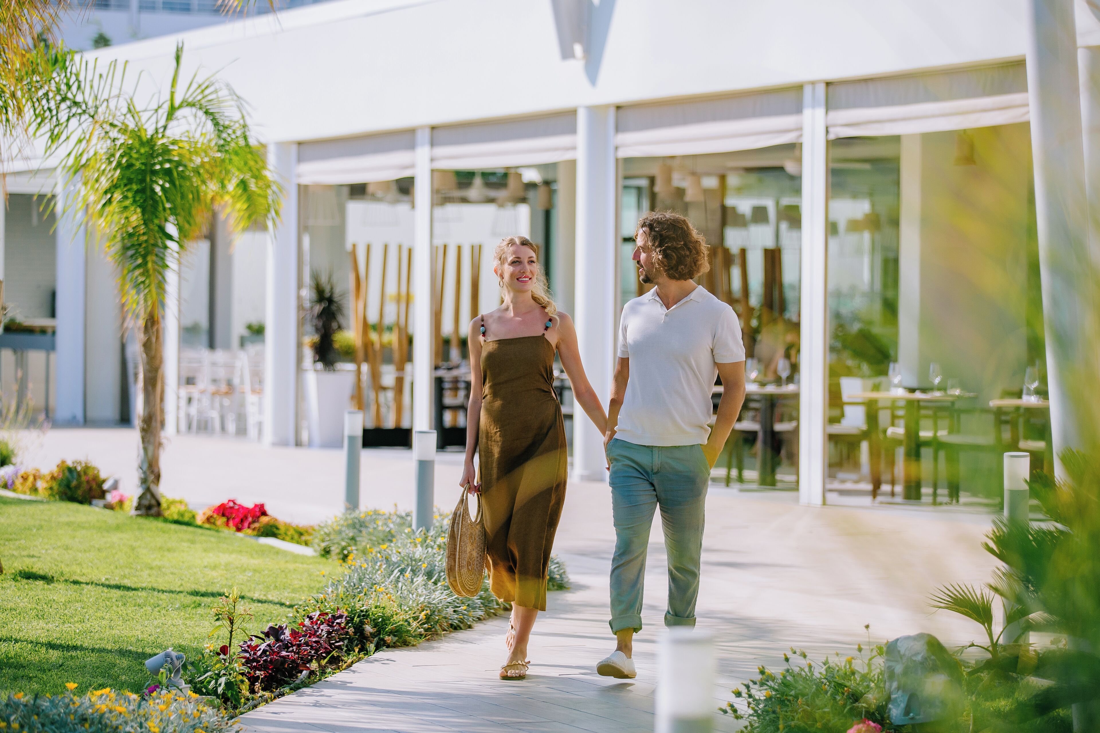 A couple walking hand in hand on a pathway with a modern building in the background.