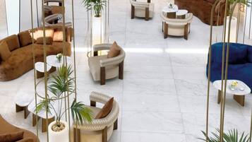A spacious lobby with multiple seating areas, including sofas and armchairs, and several potted plants.