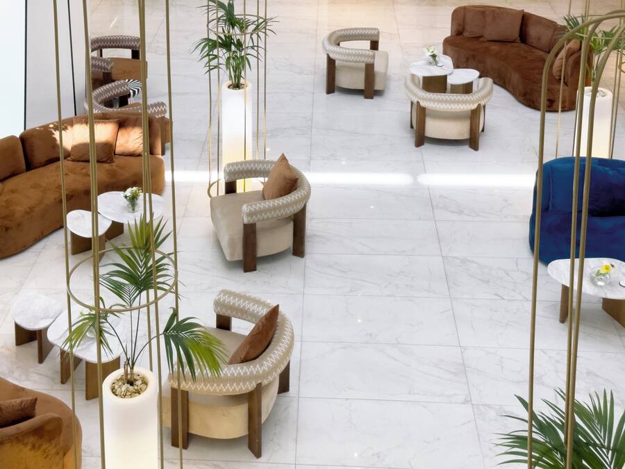 A spacious lobby with multiple seating areas, including sofas and armchairs, and several potted plants.