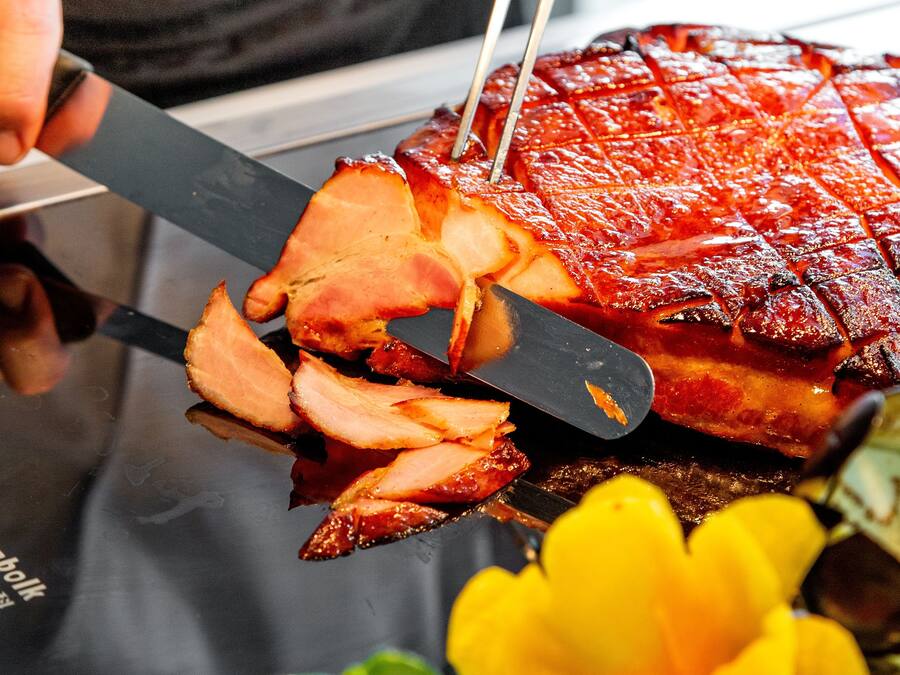 A person slicing a glazed ham with a knife.