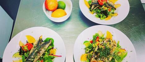 Tres platos de comida con pescado y verduras sobre una mesa de acero inoxidable.
