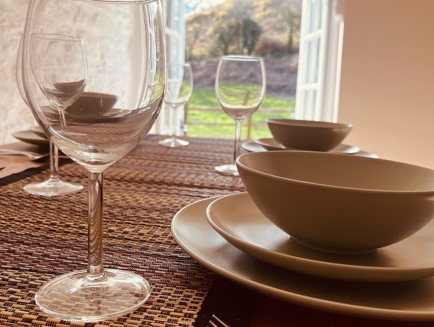 A dining table with a clear glass wine glass, a white bowl, and a plate.