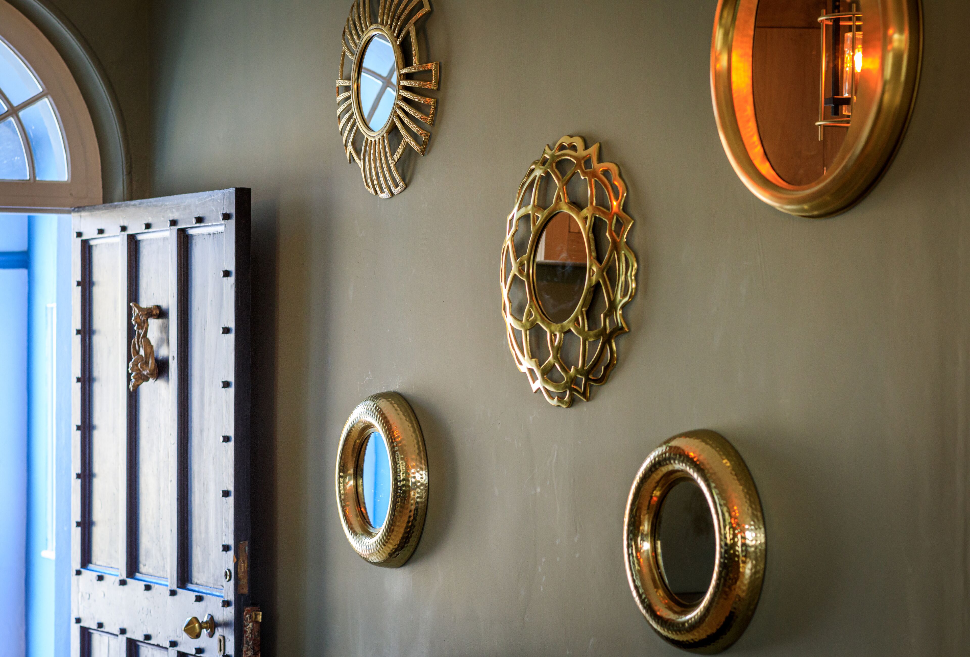 A wall with various decorative mirrors and a door with a brass handle.