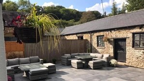A patio with stone flooring, outdoor seating, and a stone building with a sloped roof. - Picton House Hotel (Carmarthen)