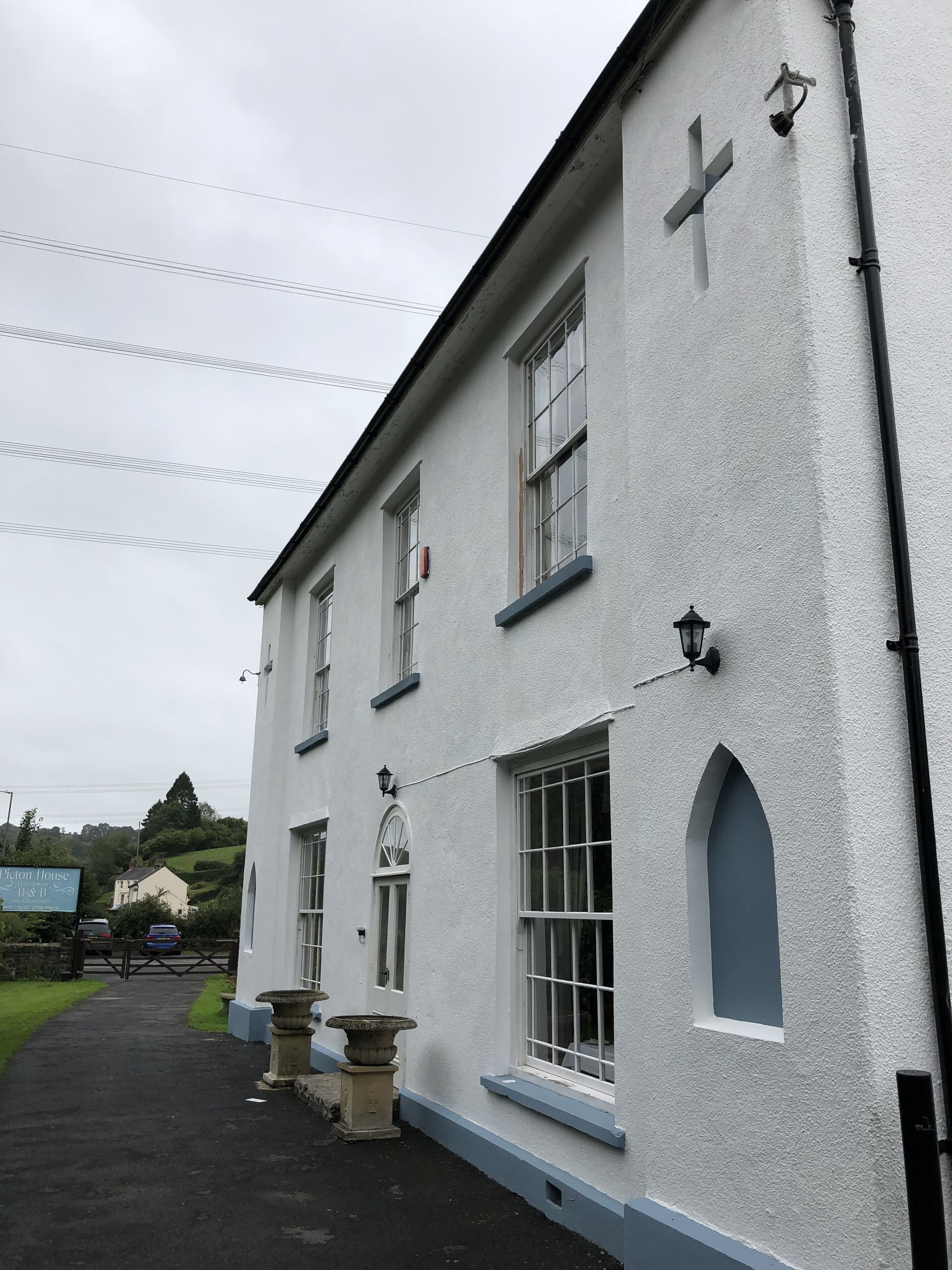 Un edificio blanco con una cruz en la pared, un letrero que dice "Pickering House Inn" y un camino pavimentado con macetas.