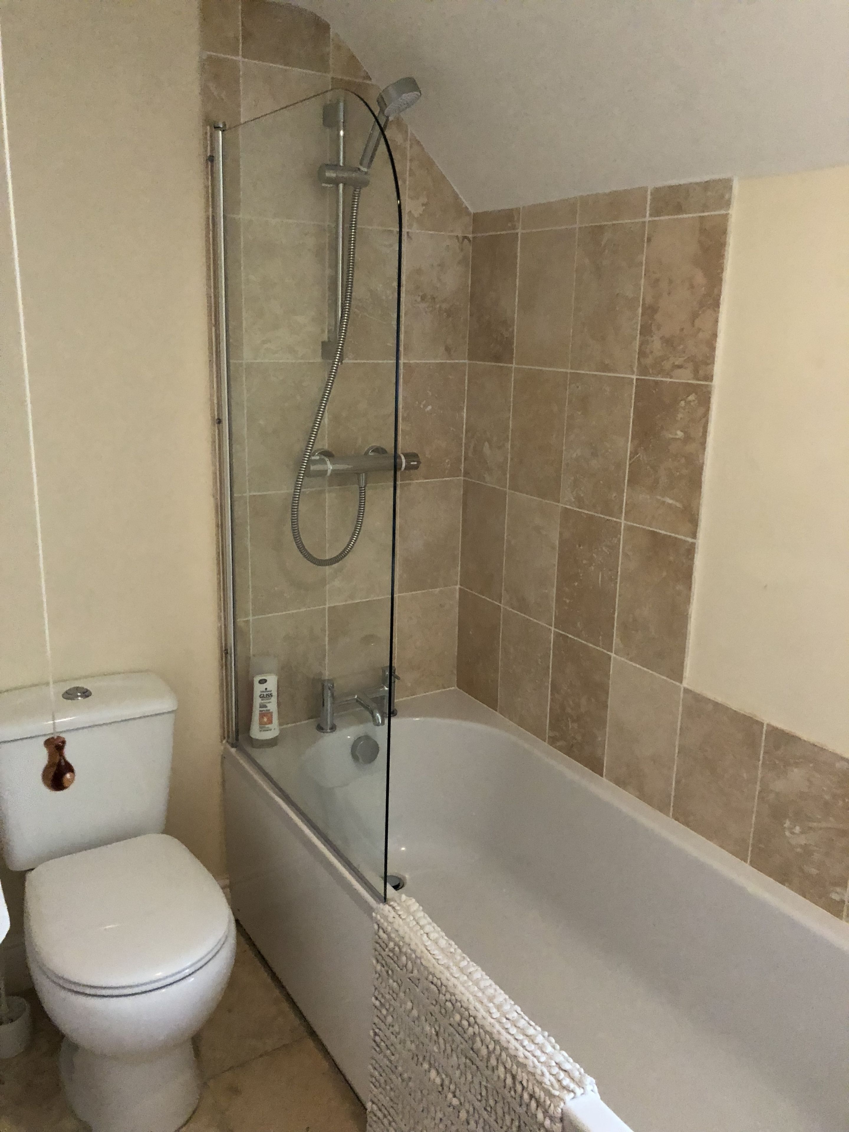 Un baño con ducha envuelta en vidrio, un inodoro blanco y paredes con azulejos color beige.