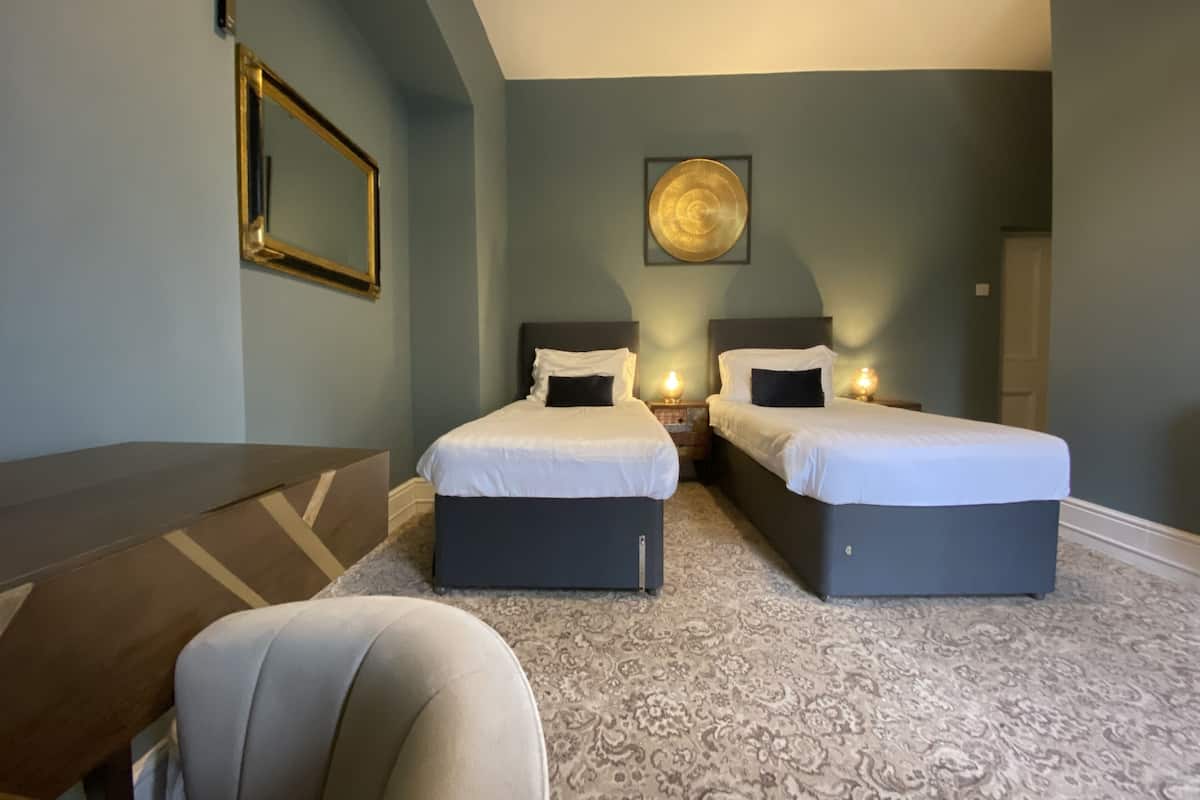 Hotellihuone, jossa on kaksi sänkyä, työpöytä, tuoli ja suuri peili.