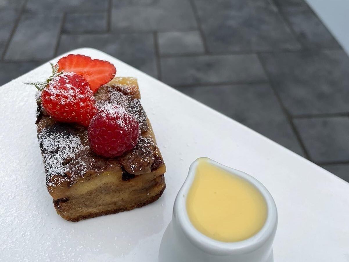 Un postre con fresas y azúcar glas sobre un plato blanco, acompañado de un pequeño cuenco de salsa.