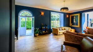 A room with a wooden floor, a sofa, a chair, a table with plants, and a door leading outside. - Picton House Hotel (Carmarthen)