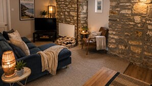 A cozy living room with a stone wall, a blue sofa, a wooden coffee table, and a television. - Picton House Hotel (Carmarthen)