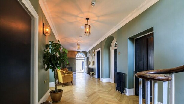 A hallway with wooden flooring, a potted plant, a chair, and a staircase with a wooden handrail. - Picton House Hotel (Carmarthen)