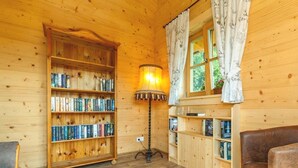 A cozy cabin interior with wooden walls and floors, a large bookshelf, a lamp, and a leather couch. - Chalet unter Weißblauem Himmel (Reit im Winkl)