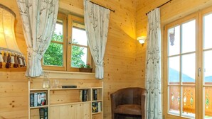 A cozy cabin interior with wooden walls, a bookshelf, a leather chair, and large windows with curtains. - Chalet unter Weißblauem Himmel (Reit im Winkl)