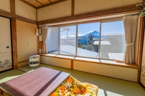 Una habitación japonesa tradicional con suelo de tatami, un futón, un calentador y vistas a una montaña.