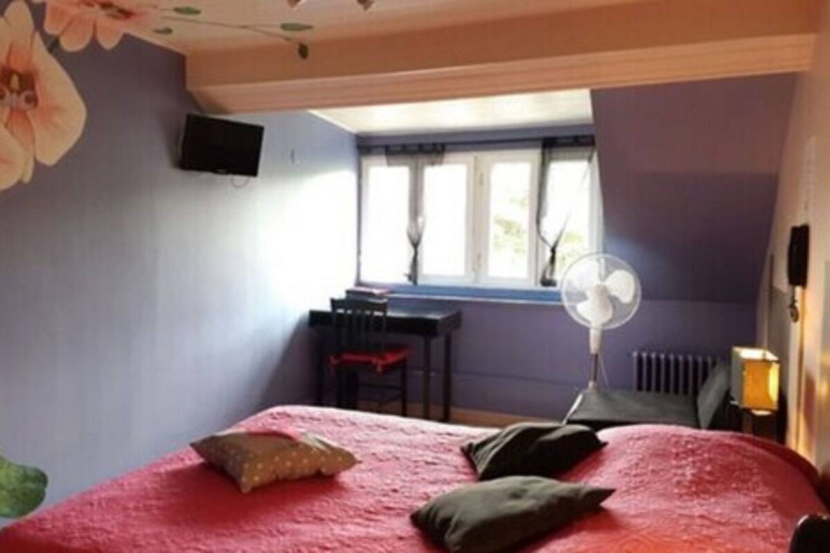 A bedroom with a bed, a desk, a chair, a window, and a wall-mounted fan.