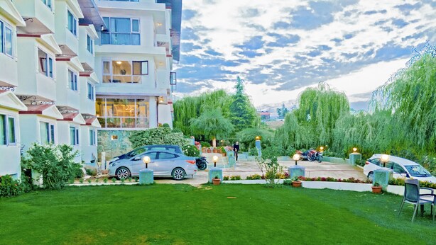 Un barrio residencial con césped cuidado, coches aparcados y un edificio con varios balcones.