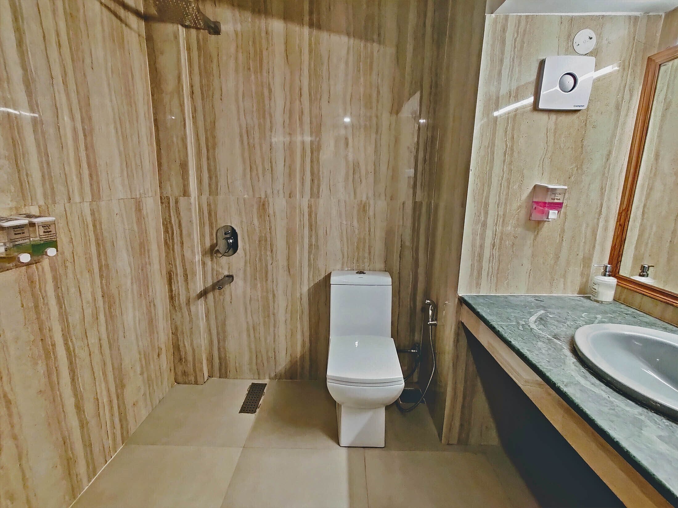 Une salle de bain avec un mur en marbre, des toilettes, une douche et un lavabo avec un miroir.